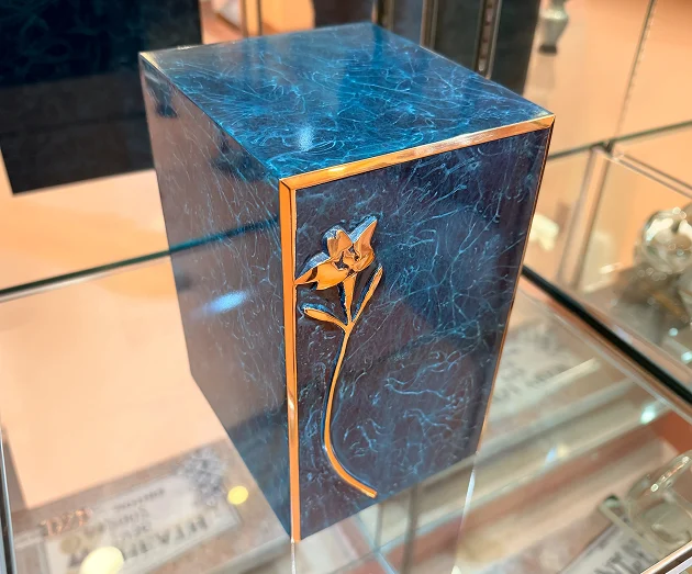 Deep blue rectangular cremation urn box with gold trim and a floral embellishment.